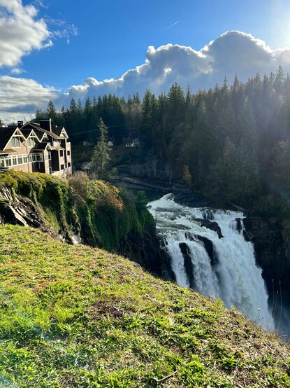 Above Snoqualmie falls with the Salish Lodge to the left and a mix of clouds and blue sky above.